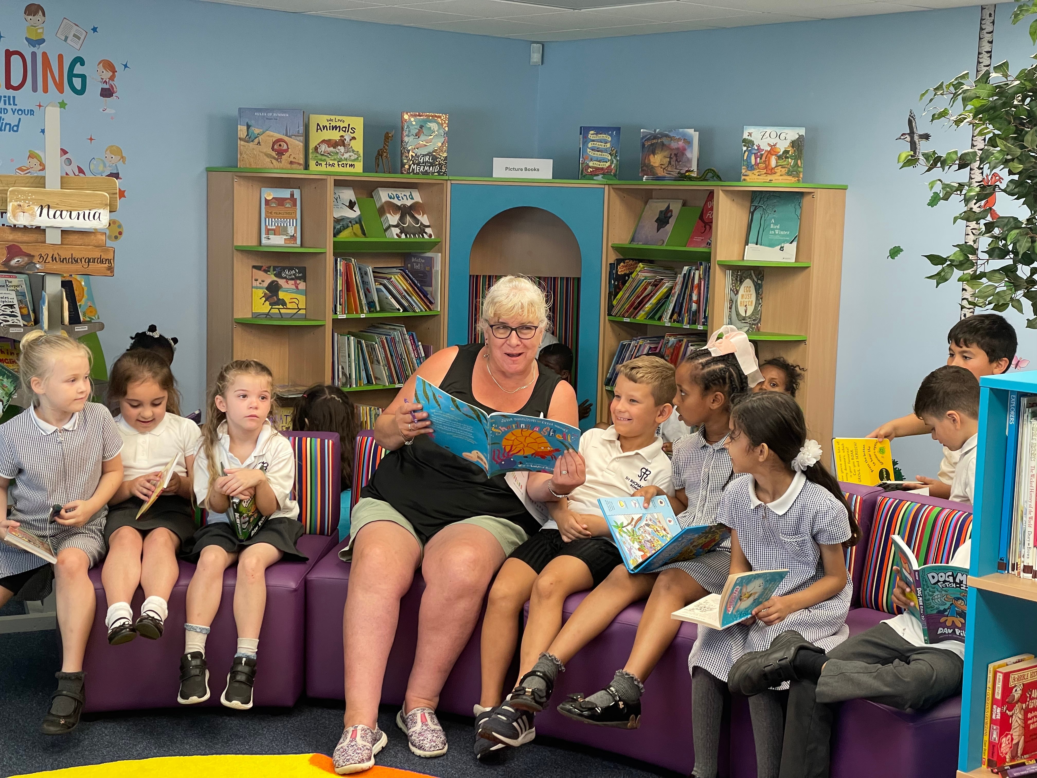 A school librarian reading to children in a brightly decorated primary school library